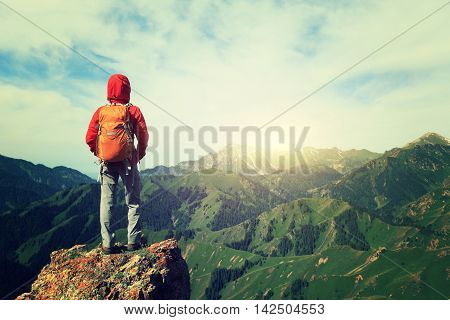 successful woman backpacker hiking on mountain peak cliff