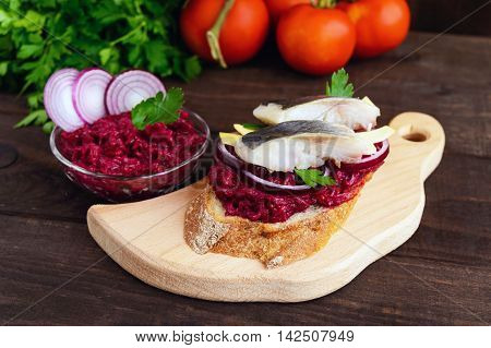 Meatless dietary sandwich: boiled beetroots purple onion salted herring and flakes of smoked cheese on a crispy baguette