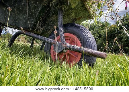 A full garden wheel barrow on long grass. Taken from a low view point showing the wheel.