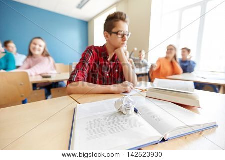 education, bullying, conflict, social relations and people concept - student boy in glasses reading book and suffering of classmates mockery at high school