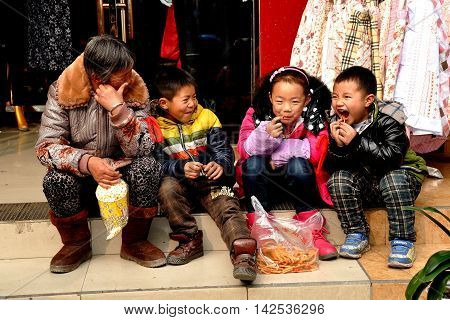 Pengzhou China - January 31 2014: Grandmother sitting on a step in front of a clothing store eating snacks with her grandson and two friends