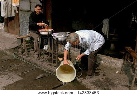 Pengzhou China - September 13, 2006: Barber uses a hose to wash a plastic pail in front of his shop on Hua Lu (Old Street)