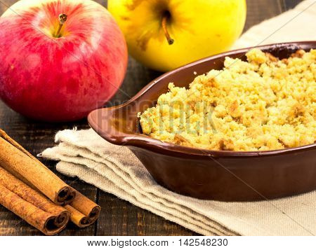 Homemade apple cramble cake with fresh apples and cinnamon sticks on rustic dark wooden background
