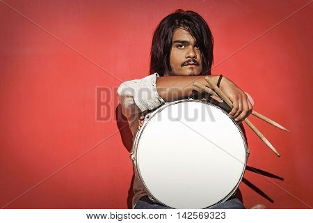 young drummer holding sticks and snare isolated on red background looking into the camera