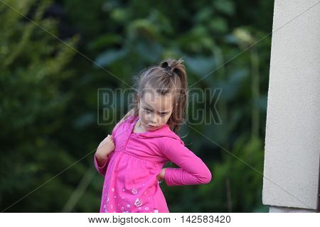 outdoor portrait of a little girl with pony tail dressed in pink shirt making angry or disappointed face