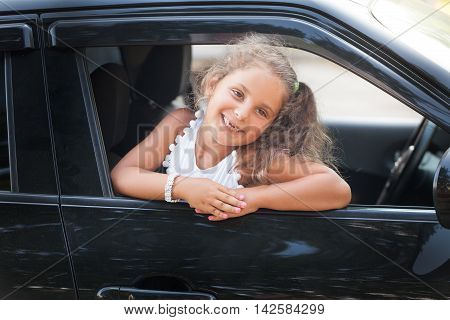 A little girl looks out the car window. She is smiling