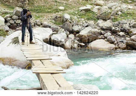 Aadventurous Photographer Aleem Zahid Khan on dangerous flooded river swat valley. standing on a bridge and capturing the moment with his camera on tripod.