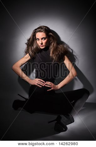 Mladý štíhlý Glamour Lady s dlouhými vousy, oblečený v černých šatech Combi sedí na podlaze, tmavě klíč