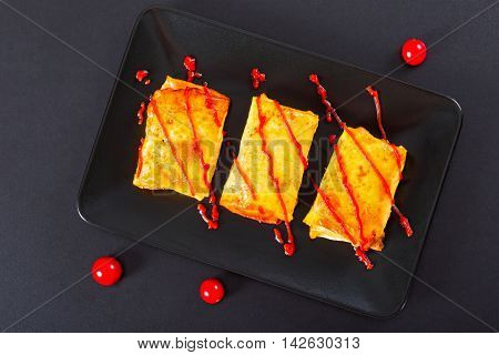 rolls of pancake or crepes stuffed with minced meat poured with ketchup on dish poured with ketchup cherry tomatoes on black background view from above close-up