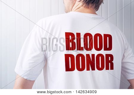 Male blood donor wearing white t-shirt person from behind posing at camera showing title at his back
