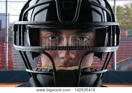 Closeup of a youth baseball catcher with backstop and grandstand in the background.
