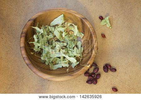 Dried flowers of linden and rose hips for herbal tea in a wooden plate. Top view.