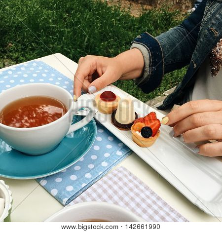 a saucer on a table and a cup of tea different delicious dessert and female hands
