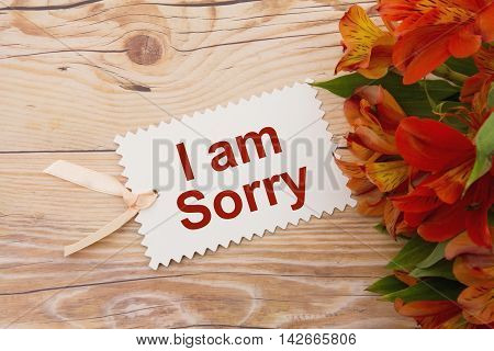 Some lilies on weathered wood with a gift tag with text I am Sorry