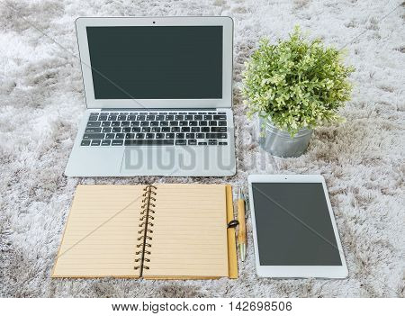 Closeup brown note book brown pen computer notebook tablet and artificial plant on gray fabric capet textured background