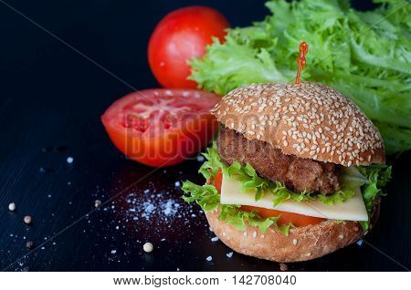 Hamburger with salad cheese tomato meat on black backdrop. Popular snack.