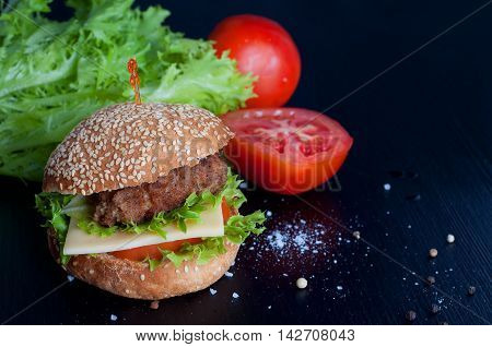 Hamburger with salad cheese tomato meat on black backdrop. Popular snack.