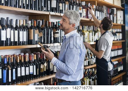 Customer And Salesman Choosing Wine Bottles In Store