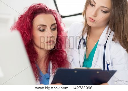 Two female doctors looking at clipboard with patient information form discussing his diagnosis and treatment. Health care medical education and service concept.