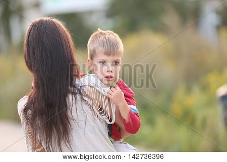 sad little blond boy carried by his mother