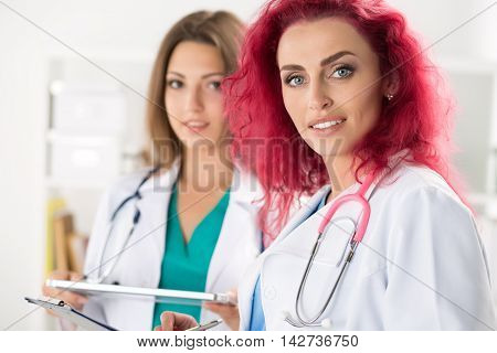 Portrait of two female doctors standing with clipboard and tablet ready to work. Health care medical service or education and teamwork concept.