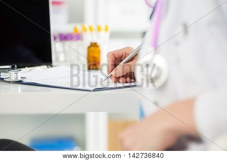 Close up view of female medicine doctors hands filling patient medical form. Physician working with paper in hospital office room. Therapeutist sitting at working table making some paperwork