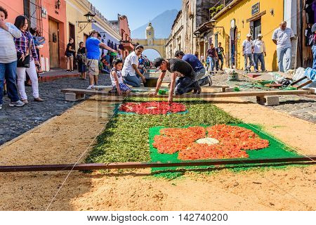 Antigua Guatemala - March 25 2016: Locals make dyed sawdust Good Friday carpets in street with arch & Agua volcano behind for procession in colonial town with most famous Holy Week celebrations in Latin America.