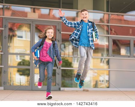 Happy children - boy and girl with books and backpacks on the first school day. Excited to be back to school after vacation. Full length outdoor portrait.