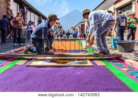 Antigua Guatemala - March 25 2016: Locals make dyed sawdust Good Friday carpets in street with Agua volcano behind for procession in colonial town with most famous Holy Week celebrations in Latin America.