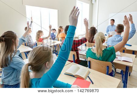 education, high school, teaching, learning and people concept - group of happy students raising hands and teacher in classroom