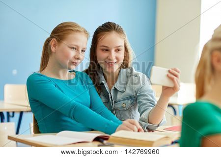 education, learning, technology, friendship and people concept - student girls with smartphone taking selfie at school lesson