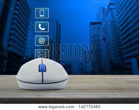 Wireless computer mouse with telephone mobile phone at and email buttons on wooden table in front of city tower background Customer support concept