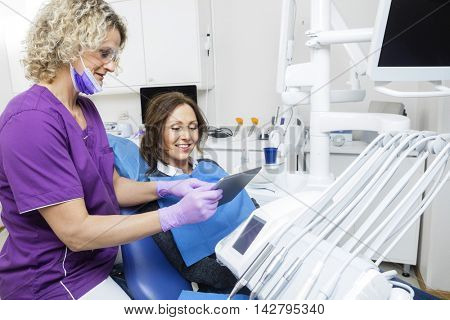 Assistant Showing Report To Patient On Tablet Computer In Dentis