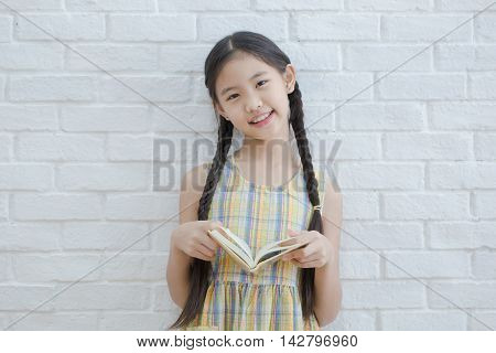 Asian girl reading story book on white brick wall