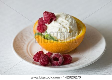Vanilla Icecream with raspberry summer dessert. Delicious sundae scoop in an orange half on a white plate. Tasty sweet dessert for summer. Serving ice cream. Serving of refreshing tropical dessert