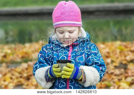 Autumn picnic portrait of little girl is holding and looking at steel thermos flask cup