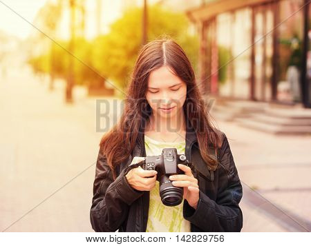 Cheerful young woman tourist watching shots in her dslr camera outdoors. Image with sunkissed effect. Vacation photography travel concept