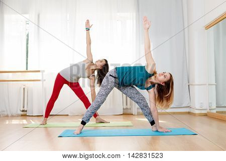 Portrait of two beautiful girls showing ashtanga vinyasa triangle yoga pose