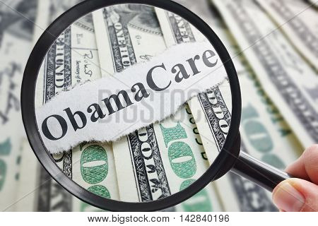 Obamacare newspaper headline on cash with magnifying glass
