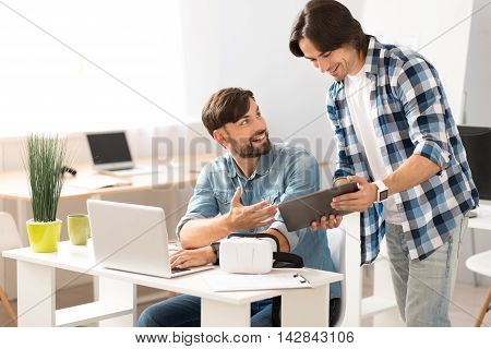 Reach common ground. Pleasant positive man sitting at the table and talking with his colleague while discussing project