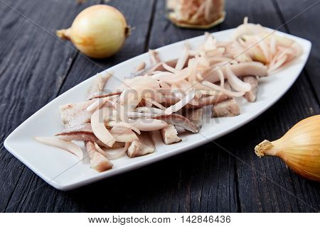 Close up of sliced herring fillets with cutted into shreds onion marinated in vinegar on white plate. Traditional home cold appetizer on wooden background with fresh onions and pickled onions in jar