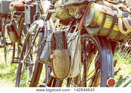Close up photo of old military bicycle with kitbag and equipments. Backpack and containers for food and drink. Vintage scene. Yellow photo filter. Equipment of german soldier in World War II.