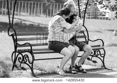 Young Family Sitting On A Park Bench. Father Holding Newborn Daughter In Her Arms.black And White Ph