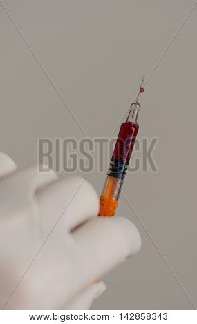 Person with latex glove pushes syringe drop at the injection needle