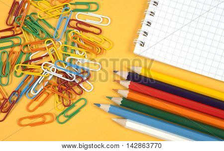 colorful paperclips, crayons and notebook on a yellow background