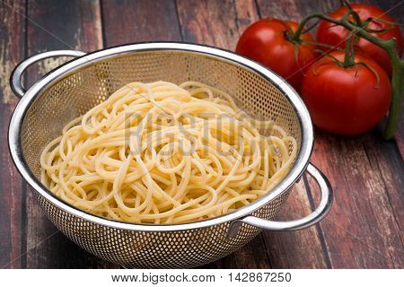 Spaghetti in a stainless steel collander on a wood surface