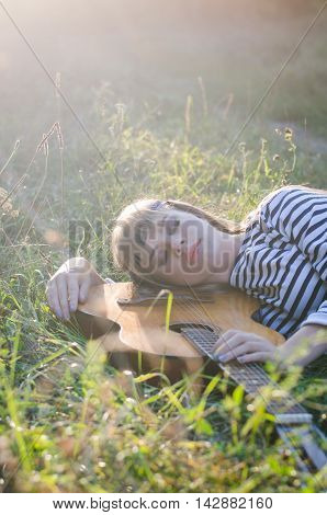 Hippie-style girl posing with a guitar on a hot summer evening she is wearing a head band stripy frock and skinny jeans