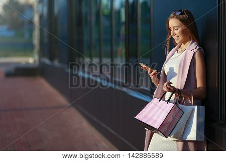 Smiling girl with shopping bags and looking in the phone