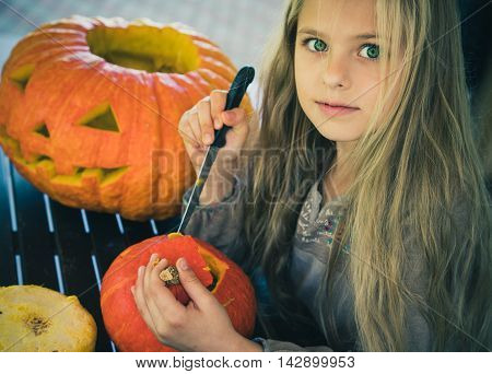 Beautiful girl with green eyes cut a pumpkin for Halloween. Symbol.