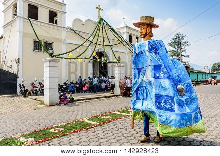 Parramos Guatemala - May 29 2016: Giant puppet folk dancer called a gigante walks past church & processional carpet during Corpus Christi mass.